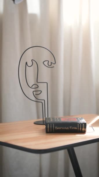 Журнальный столик с книгой и абстрактной фигурой головы на фоне белой кирпичной стены — стоковое видео