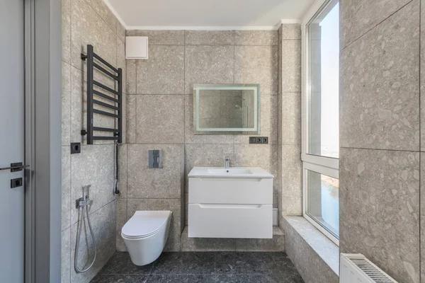  Geniş pencereli tuvalet, tuvalet ve aynalı lavabo.