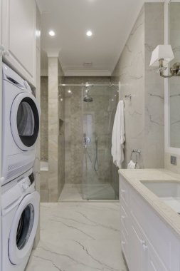 Duvarlarında mermer, çamaşır makinesi ve duşu olan parlak bir banyo.