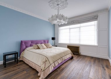 Büyük bir pencerenin yanındaki mavi bir odada büyük mor bir yatak. Önde cam bir bölme var. Yüksek kalite fotoğraf