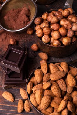 Durgun hayat. Ön planda, kabuklu fındık ve bademlerle kaşık ölçen antika metaller, kakao tozu ve koyu çikolata parçaları..