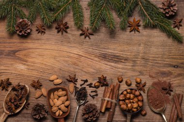 Üst manzara, desenli ahşap arka planda, çam kozalaklı dallar, çeşitli baharatlar ve kurutulmuş meyveler. Metnin için boşluk. Noel sahnesi.