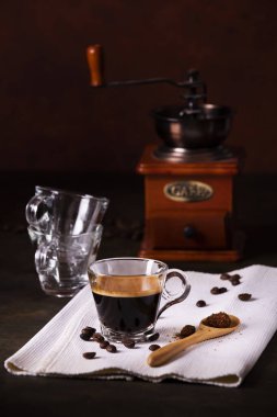 Ön planda, cam bardakta sıcak kahve, ve çiğ kamış şekerli ahşap kaşık, arka planda antika bir kahve öğütücüsü. durgun hayat