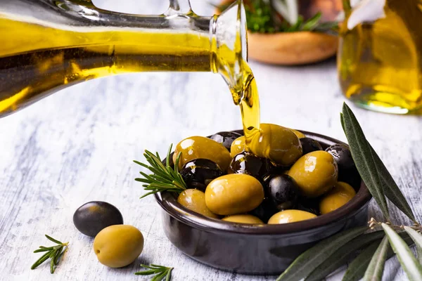 Ön planda, biberiye aromalı zeytinlerin olduğu bir kaseye ekstra saf zeytinyağı dökülüyor.