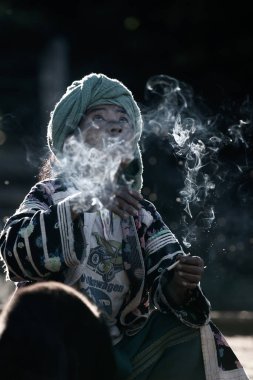 Chiang Mai, Tayland - 21 Aralık 2010: Geleneksel kıyafet giymiş, güneş ışığında sigara içen yaşlı bir Lahu kabilesi kadını. Omkoi.