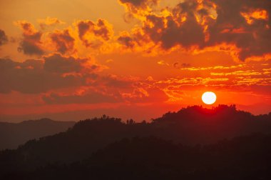 Tayland-Myanmar sınırı yakınlarındaki dağların üzerinden parlayan güneş batıyor. Gün batımında dramatik bulutlar. Siluet.