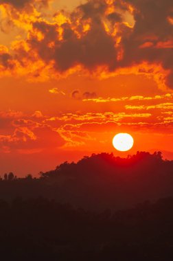 Tayland-Myanmar sınırı yakınlarındaki dağların üzerinden parlayan güneş batıyor. Gün batımında dramatik bulutlar. Siluet.
