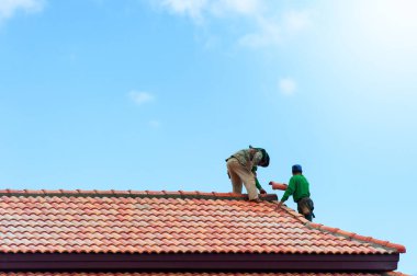 İki Asyalı müteahhit çatının tepesine inşaat halindeki kiremitleri yerleştiriyor. Çatı inşaatı.