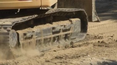 Kazı makinesi zinciri bir inşaat alanındaki tozlu yolda ilerliyor.