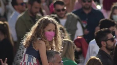 Girl with face mask on man's shoulders in a crowd