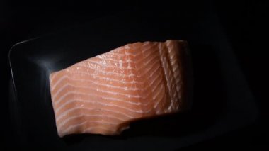 Raw salmon fillet steak on a black tray gyrating with intimate light, top view