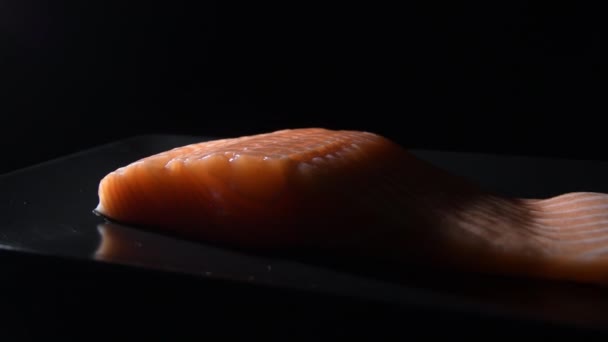 新鲜的生鲑鱼片在一个黑色盘子里旋转着 有强烈的光 — 图库视频影像