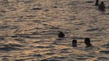 People swimming in a calm beach at sunset