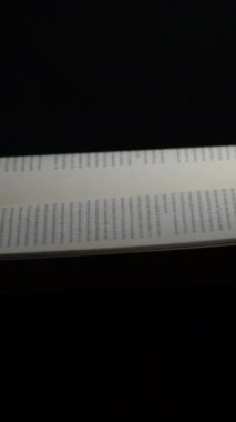 Siyah arkaplanı ve rotasyonu olan açık kitapların sayfaları. 4K Dikey