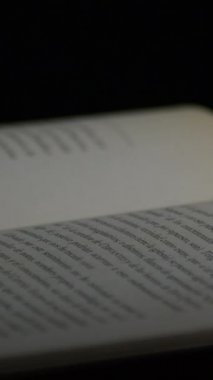 Siyah arkaplanı ve rotasyonu olan açık kitapların sayfaları. 4K Dikey