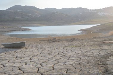 Cracked land by drought with a small boat in the shore of a lake
