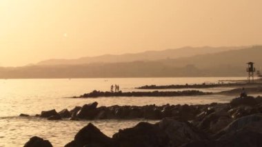 Çocuklar gün batımında plajın kayalarında oynuyorlar.