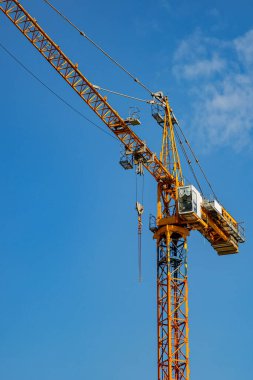 Güneşli bir günde mavi gökyüzünün arka planında inşaat vinci yük kaldırır.