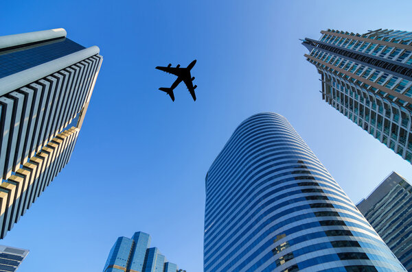 Silhouette aircraft flying over modern building in the business district.