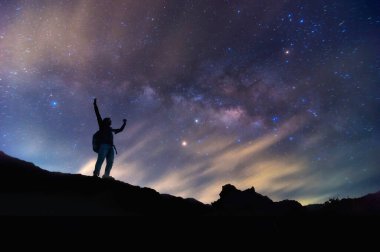 Samanyolu 'yla manzara. Gece gökyüzü yıldızlarla ve dağda duran mutlu bir adamın silüetiyle, Başarı ya da kazanan, lider konsepti. Gürültülü yüksek izo.