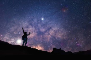 Samanyolu 'yla manzara. Gece gökyüzü yıldızlarla ve dağda duran mutlu bir adamın silüetiyle, Başarı ya da kazanan, lider konsepti. Gürültülü yüksek izo.