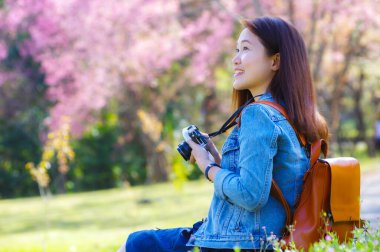 Klasik fotoğraf makinesi kullanan genç, güzel Asyalı bir gezgin. Bahar kiraz çiçeklerinin ortasında gülümseyen bir mutlu fotoğraf çek. Seyahat yaşam tarzı, dünya gezgini, Asya seyahat fikri..