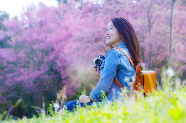 Klasik fotoğraf makinesi kullanan genç, güzel Asyalı bir gezgin. Bahar kiraz çiçeklerinin ortasında gülümseyen bir mutlu fotoğraf çek. Seyahat yaşam tarzı, dünya gezgini, Asya seyahat fikri..