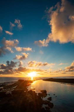 Des Roches Adası, Seyşeller 'de, ufukta bulutlar ve güneş olan okyanus kıyısında tropik bir günbatımı.