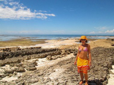 Genç bir kadın, tropikal bir adada bir pareo ile sahilde yürüyor.