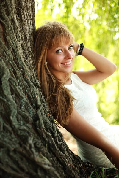Beautiful young woman resting under big tree — Stock Photo, Image