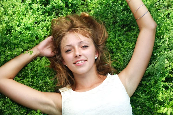 Beautiful young blonde girl in park lying on the green grass — Stock Photo, Image