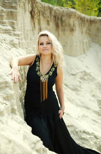 Moda blond dziewczyna w długiej czarnej sukni, pozowanie piasek pustyni — Zdjęcie stockowe