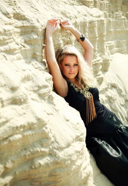 Mode blond meisje in lange zwarte jurk poseren in zand woestijn met handen omhoog — Stockfoto