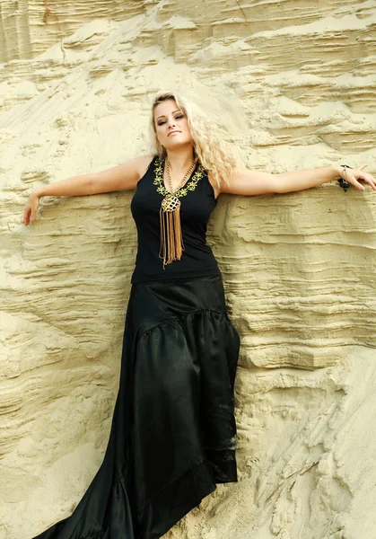 Moda chica rubia en vestido largo negro posando en el desierto de arena con los ojos cerrados —  Fotos de Stock