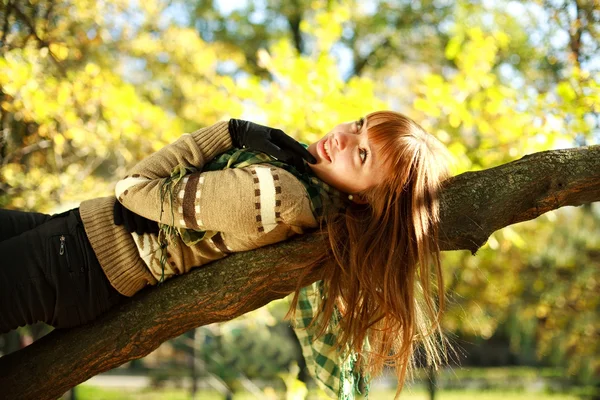 Outdoors portrait of autumn smiling girl lying on tree — Stock Photo, Image