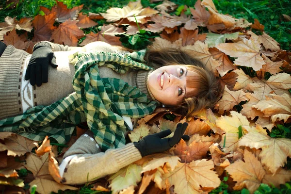 Fille heureuse allongée sur des feuilles jaunes à l'extérieur — Photo