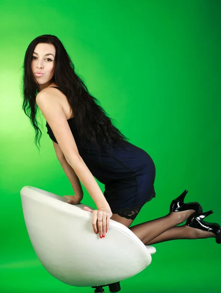 Sensuality young brunette on white chair in studio, on green background — Stock Photo, Image