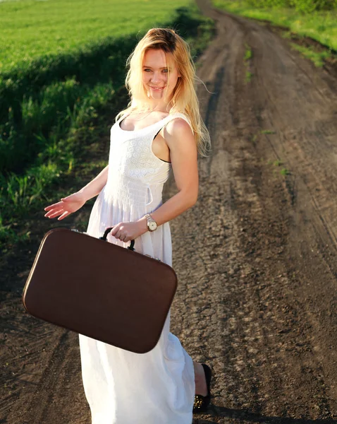 Prachtige blond meisje in lange witte jurk met koffer — Stockfoto