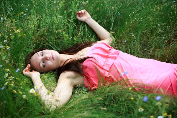 Vacker ung flicka sover på ängen i grönt gräs — Stockfoto