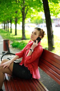 telefonda konuşurken bir bankta bir parkta oturan genç kadın