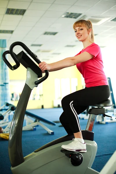 Sportliches süßes Mädchen, das auf dem Fahrrad in der Turnhalle trainiert — Stockfoto