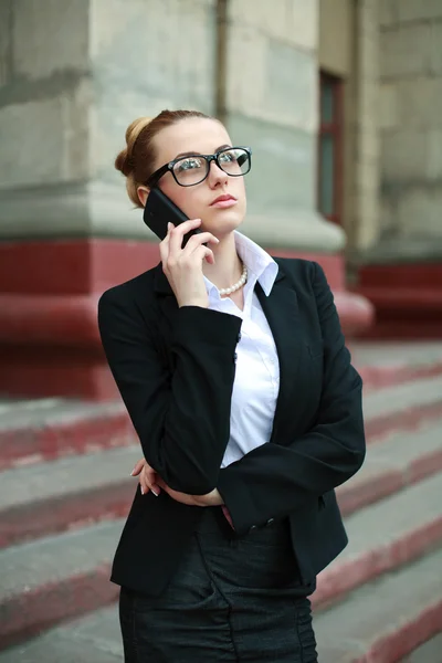 Jovem mulher de negócios em terno preto e óculos falando no telefone — Fotografia de Stock