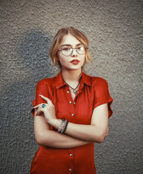 赤いドレスとメガネのスマートエレガントな若い女性は コンクリート壁 レトロな肖像画のイメージの背景に カメラに思慮深く見えます — ストック写真