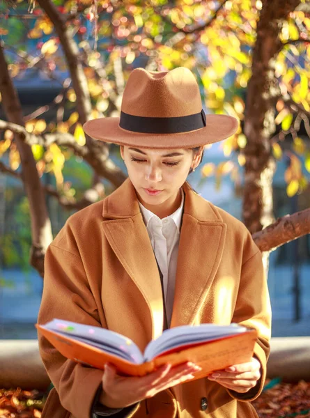 街の公園でコートや帽子に身を包んだ少女は カラフルな木の下で本を読み 屋外で学ぶ — ストック写真