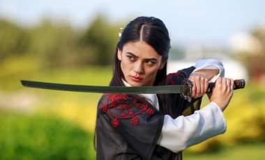 Geleneksel kimonolu genç Asyalı kadın yeşil yaz bahçesinde Katana Kılıçlı Samuray Savaşçısı kızla yakın plan bir dövüş duruşu içinde eğitim alıyor.