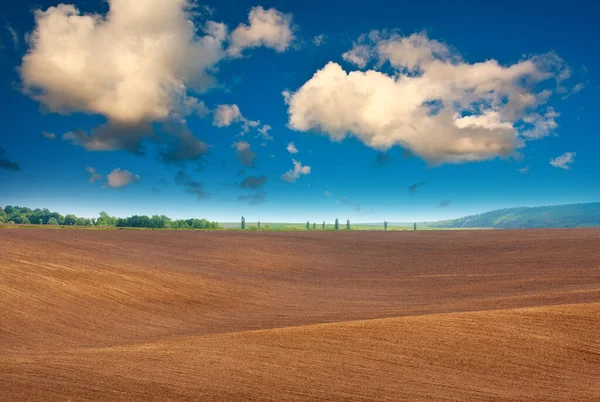 Plowed agricultural field soil against the background of a rural landscape and a mystical sky with white clouds