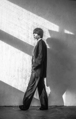 Düşünceli, çıplak ayaklı, takım elbiseli genç bir kadın, güneşli bir duvarın arkasında yürüyor, konsept portresi, siyah beyaz fotoğraf.