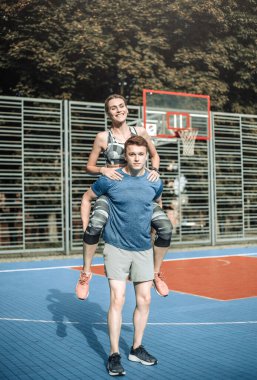 Genç spor çifti basketbol sahasında kucaklaşırken eğleniyor, dışarıda boş zaman aktiviteleri yapıyor.