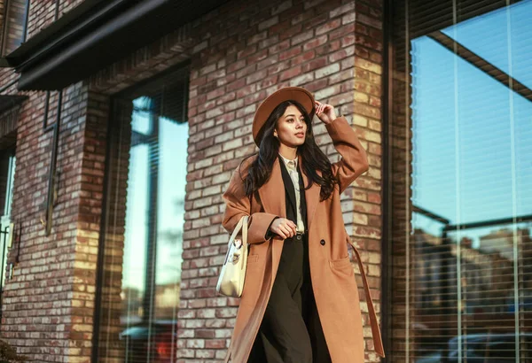 長いベージュのコートと帽子のアジアのビジネス女性は レンガの壁 古典的なレトロなスタイルを背景に ロフトスタイルで通りを歩いて — ストック写真