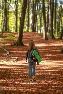Sırt çantasıyla gezen, gezen, gezen, güneşli bir orman parkında yalnız başına gezen düşünceli bir kız.